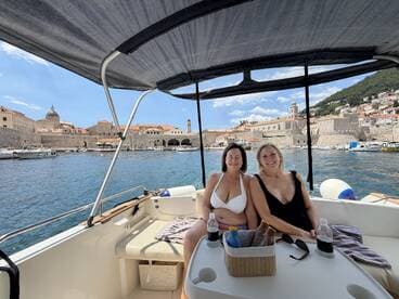 Two friends relax on a boat with drinks, enjoying the scenic view of the historic waterfront — a perfect moment for a summer getaway.