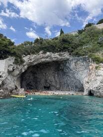 A stunning view of a beach nestled within a cave, with groups of people enjoying the crystal-clear waters — a perfect destination for swimming and exploration.