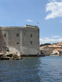 A scenic view of a historic fortress along the coastline, with visitors exploring the area — a perfect backdrop for boat tours in Dubrovnik.