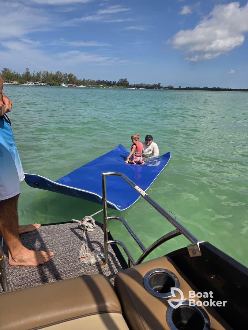 A child and an adult enjoy a fun moment on a floating mat in the clear waters, showcasing a perfect family day out on the boat.
