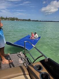 A child and an adult enjoy a fun moment on a floating mat in the clear waters, showcasing a perfect family day out on the boat.