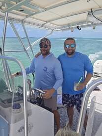 Two friends enjoy a day on the water, with one steering the boat and the other holding a drink — a perfect snapshot of fun and relaxation on a boating adventure.