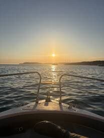A serene sunset view from the bow of a boat, capturing the tranquil waters and distant coastline — perfect for evening cruises.