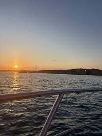 A serene sunset view from the deck of a boat, showcasing the tranquil waters and distant land, perfect for capturing the beauty of evening cruises.