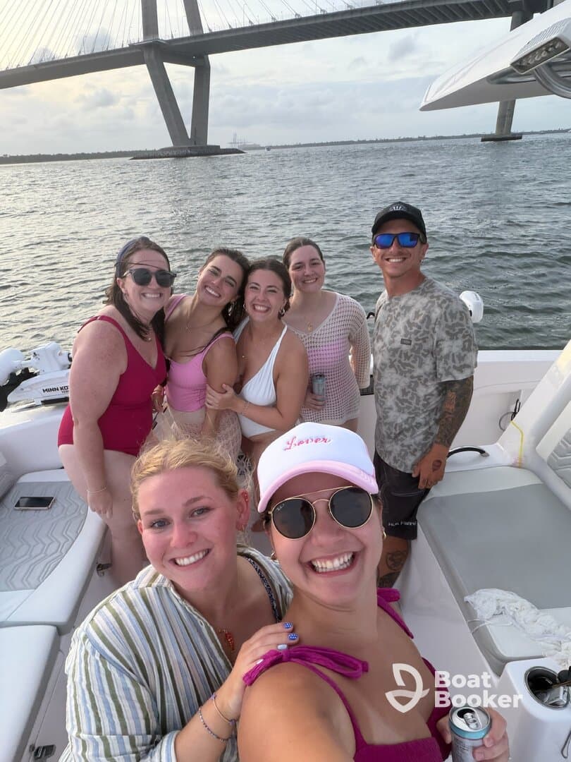 A joyful group of friends poses for a selfie on a boat, celebrating their time together under a bridge — perfect for summer outings and memorable adventures on the water.