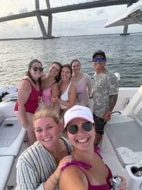 A joyful group of friends poses for a selfie on a boat, celebrating their time together under a bridge — perfect for summer outings and memorable adventures on the water.