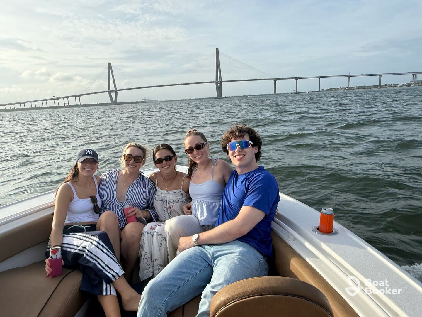 A cheerful group of friends enjoys a day on the water, posing for a photo with a stunning bridge in the background — perfect for memorable boating adventures.