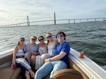 A cheerful group of friends enjoys a day on the water, posing for a photo with a stunning bridge in the background — perfect for memorable boating adventures.