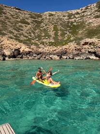 A couple enjoys paddleboarding in crystal-clear waters, surrounded by stunning rocky cliffs — a perfect day for adventure and fun in the sun.