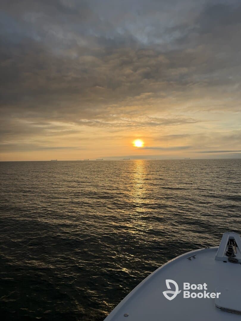 A serene sunset view from the bow of a boat, showcasing the tranquil waters and a hint of the boat's name — perfect for peaceful evening cruises.