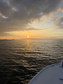 A serene sunset view over the water with the bow of a boat in the foreground, creating a picturesque scene perfect for evening cruises.