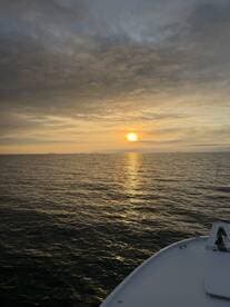 A serene sunset view from the bow of a boat, showcasing the tranquil waters and a hint of the boat's name — perfect for peaceful evening cruises.