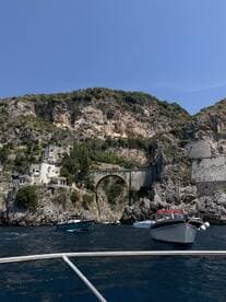 A stunning view of boats navigating near a picturesque coastline with rocky cliffs and a historic bridge, perfect for exploring scenic destinations.