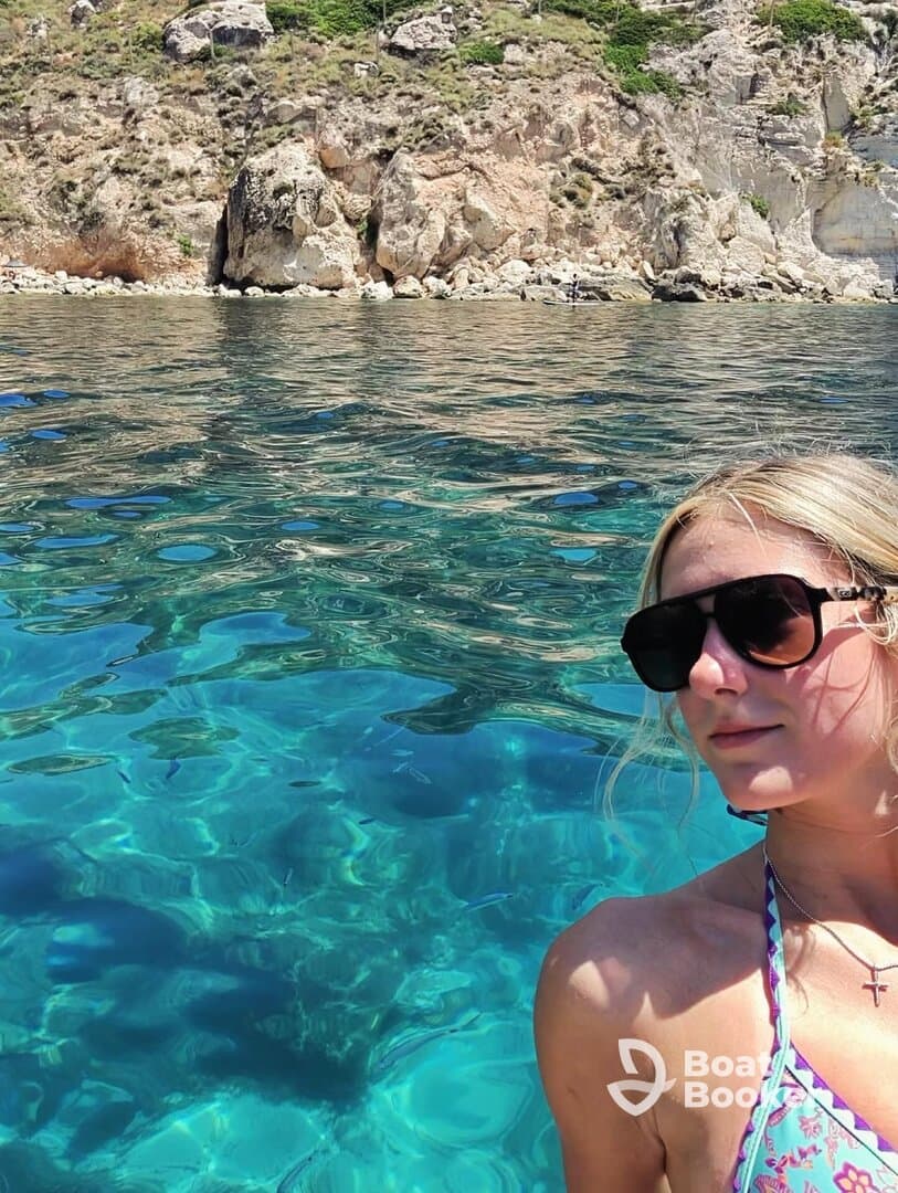 A woman enjoys the crystal-clear waters while swimming near a rocky coastline, capturing the essence of a perfect beach day.