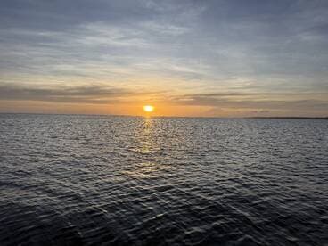 A serene sunset over calm waters, creating a picturesque view perfect for evening boat cruises or relaxation on the water.