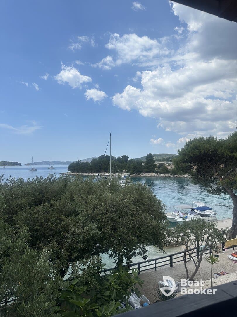 A picturesque view of a harbor with sailboats anchored, framed by lush greenery and a clear blue sky — a perfect representation of a serene coastal getaway.