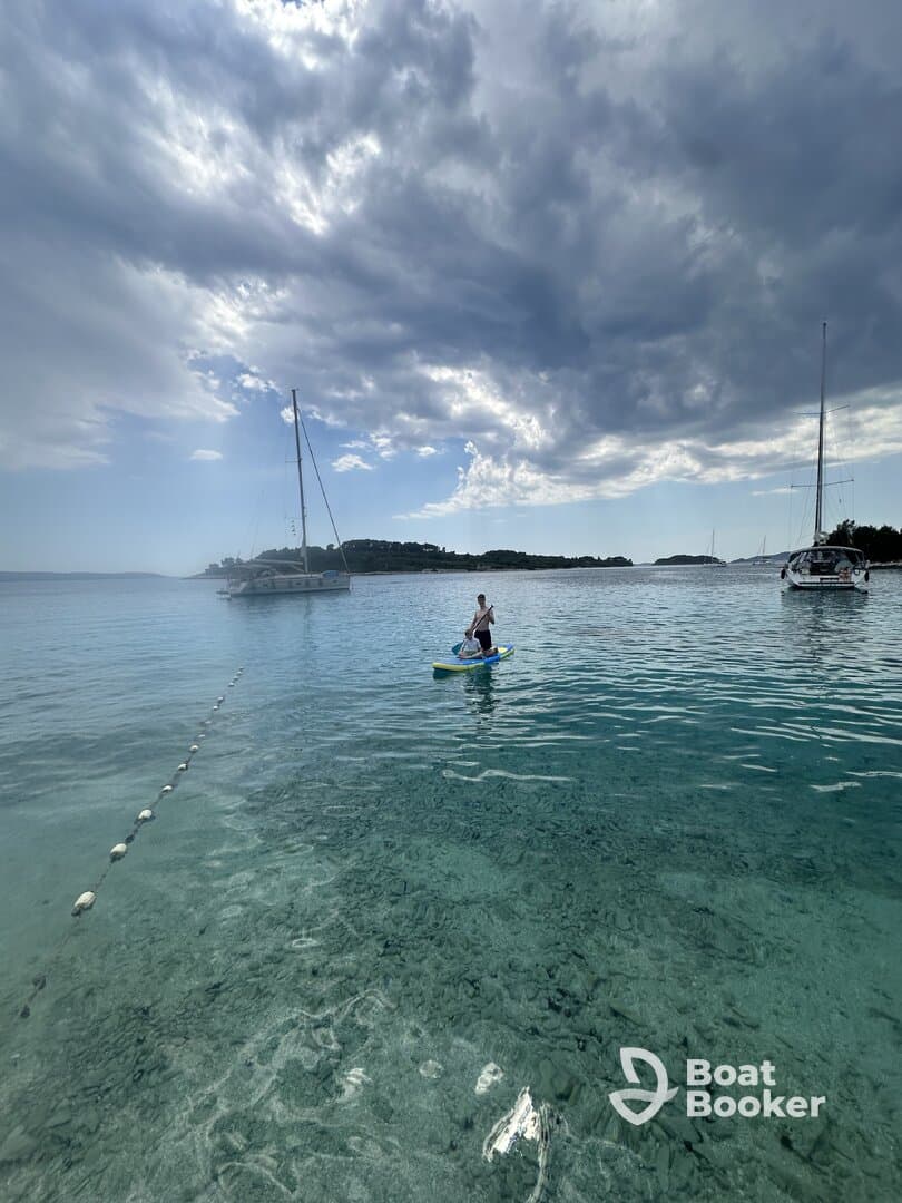 A paddleboarder glides across crystal-clear waters with sailboats in the background, showcasing a perfect day for water activities and exploration.