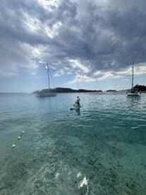 A paddleboarder glides across crystal-clear waters with sailboats in the background, showcasing a perfect day for water activities and exploration.