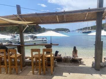 Two guests relax on the beach, enjoying the serene view of boats anchored in the turquoise waters — a perfect spot for unwinding and soaking up the sun.