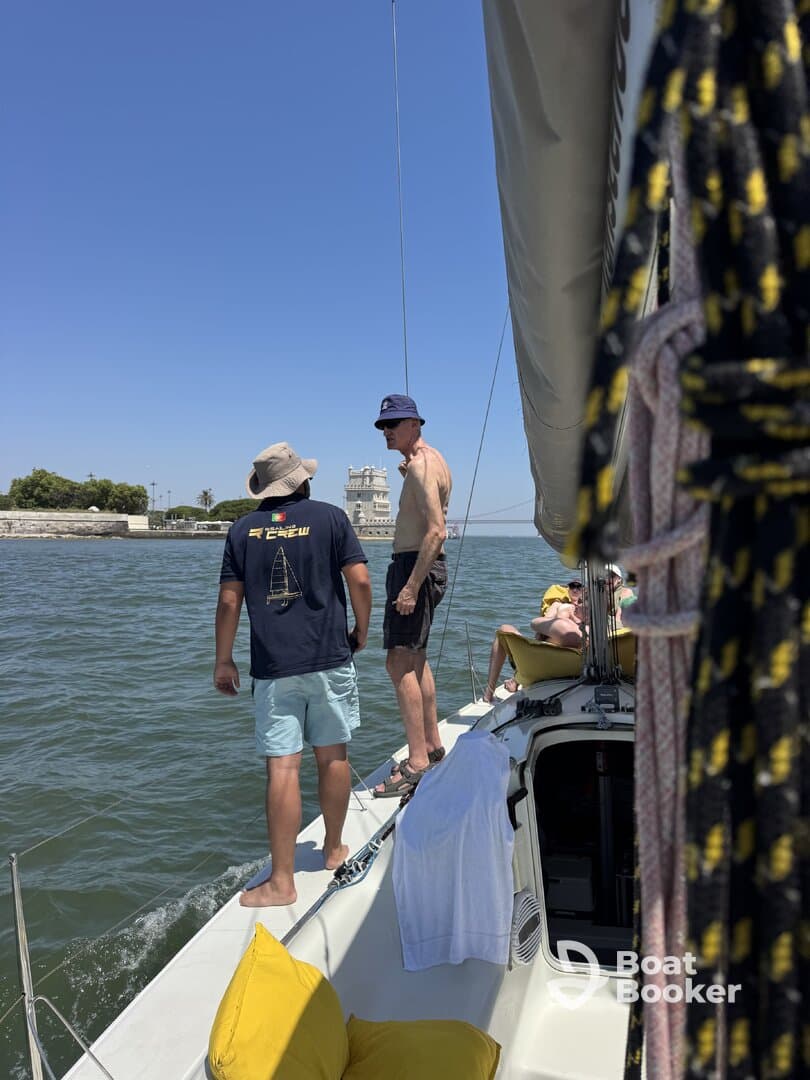 A group of friends enjoys a sunny day sailing, with one person standing at the edge of the boat, creating a lively atmosphere on the water.