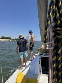 A group of friends enjoys a sunny day sailing, with one person standing at the edge of the boat, creating a lively atmosphere on the water.