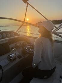 A woman enjoys the sunset while steering a boat, creating a serene atmosphere perfect for evening cruises on the water.