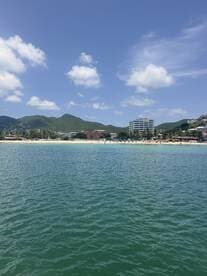 A picturesque view of a beach with clear waters and lush mountains in the background, showcasing a vibrant coastal scene perfect for relaxation and water activities.