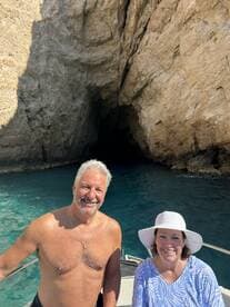 A cheerful couple poses on their boat near a stunning cave, showcasing the beauty of their boating adventure.