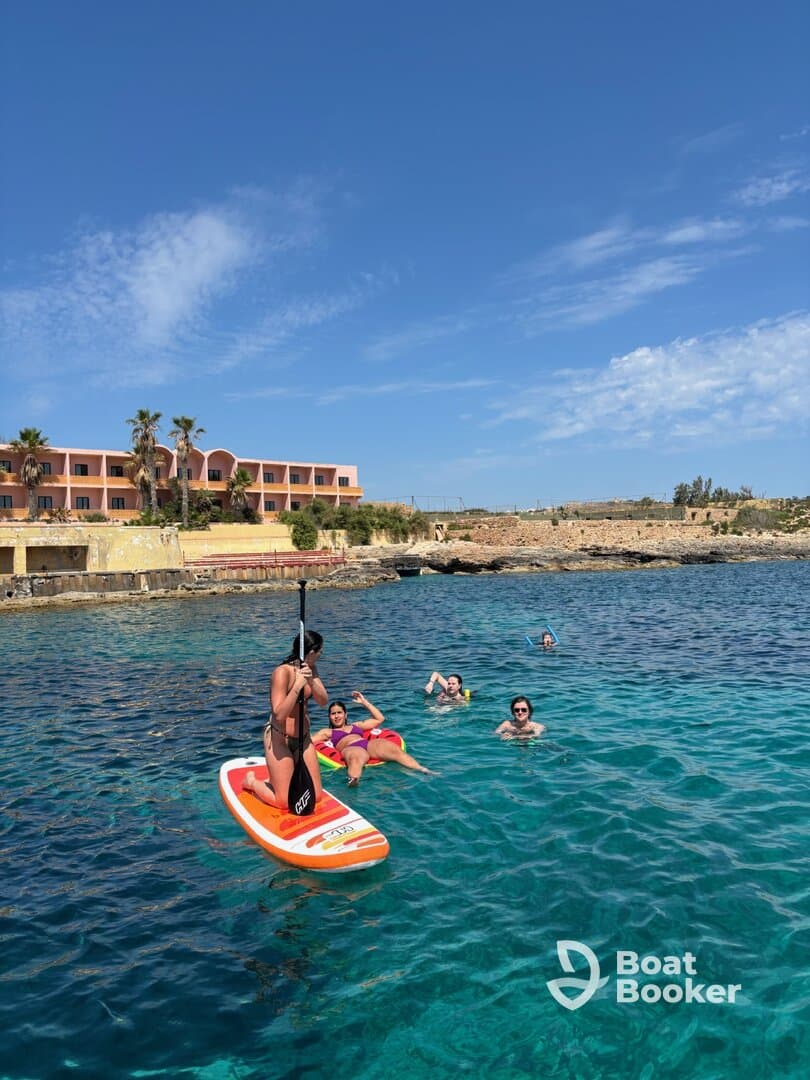 A group enjoys a sunny day by the water, with one person paddleboarding while others swim nearby — a perfect scene for summer fun and water activities.