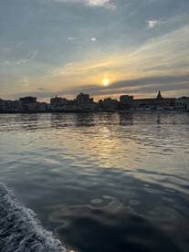 A stunning sunset reflects on the calm waters, showcasing the beautiful coastline and city skyline — perfect for capturing serene moments on the water.