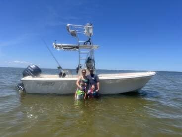A family enjoys a sunny day in the water next to their boat, creating lasting memories during their outdoor adventure.