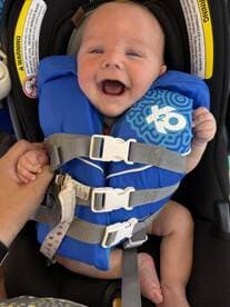 A joyful baby in a life jacket, ready for a boating adventure. Safety first for little ones on the water!