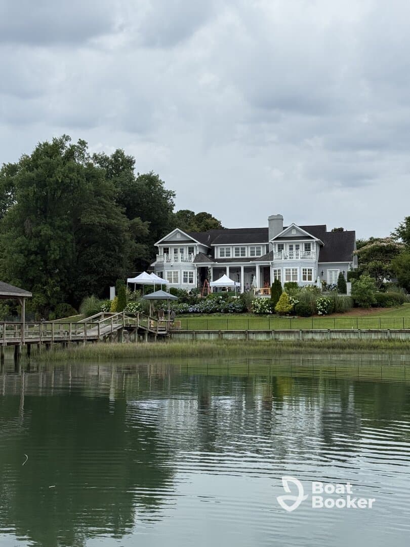 A scenic view of a waterfront house with a dock, surrounded by greenery and cloudy skies, creating a tranquil atmosphere.