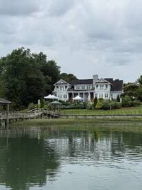 A scenic view of a waterfront house with a dock, surrounded by greenery and cloudy skies, creating a tranquil atmosphere.