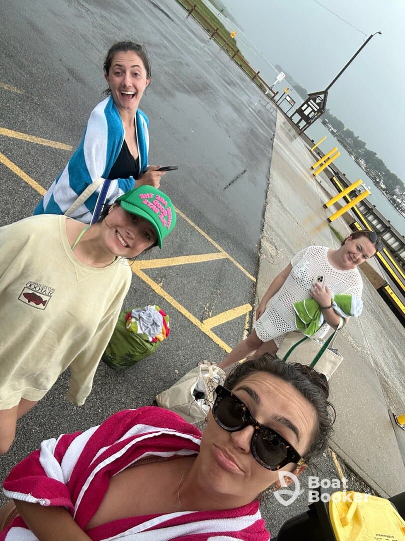 A cheerful group of friends poses for a fun selfie at the dock, capturing the excitement of their boating adventure despite the rainy weather.