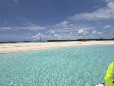 A stunning view of a secluded beach with crystal-clear turquoise waters and a distant sailboat, perfect for showcasing the beauty of island destinations.