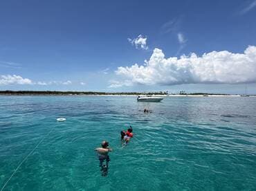 A group enjoys a fun day of snorkeling and swimming in crystal-clear waters, with a boat anchored nearby, perfect for a beach adventure.