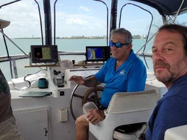 Inside view of the boat's helm with two men engaged in conversation, showcasing the navigation equipment and cabin space.