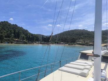 A serene view from the deck of a yacht, showcasing the turquoise waters and lush greenery of the coastline — perfect for a relaxing day on the water.