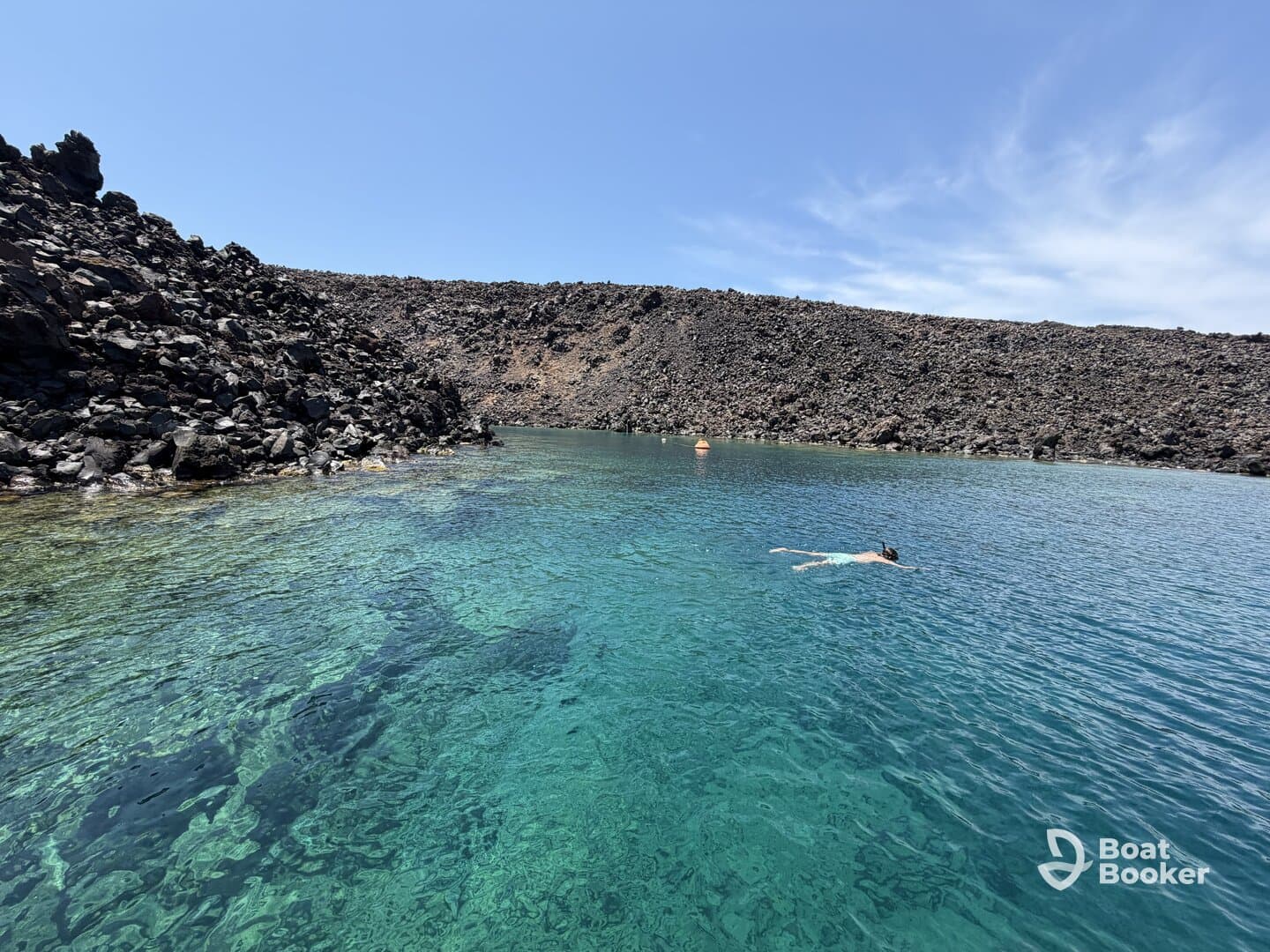 A swimmer enjoys the crystal-clear waters surrounded by a dramatic rocky coastline, showcasing the beauty of a secluded natural swimming spot.