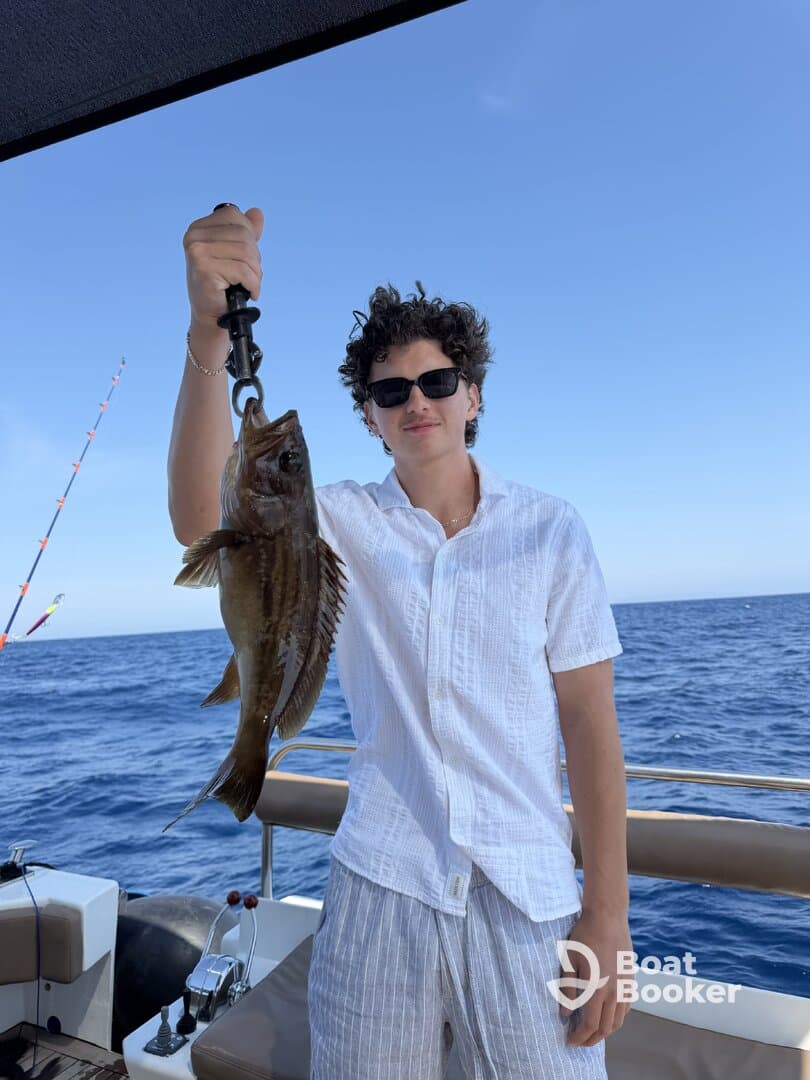 A young man proudly displays his catch while fishing on a boat in the open ocean — a perfect moment for fishing enthusiasts.