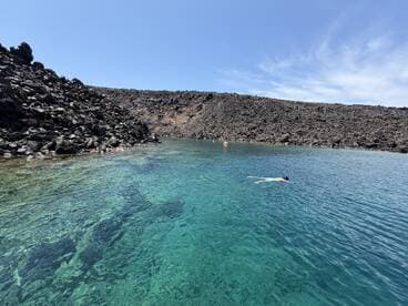 A swimmer enjoys the crystal-clear waters surrounded by a dramatic rocky coastline, showcasing the beauty of a secluded natural swimming spot.