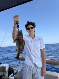 A young man proudly displays his catch while fishing on a boat in the open ocean — a perfect moment for fishing enthusiasts.