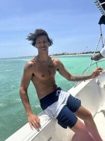 A young man enjoys a sunny day on the boat, capturing the essence of a perfect day at sea with clear turquoise waters in the background.