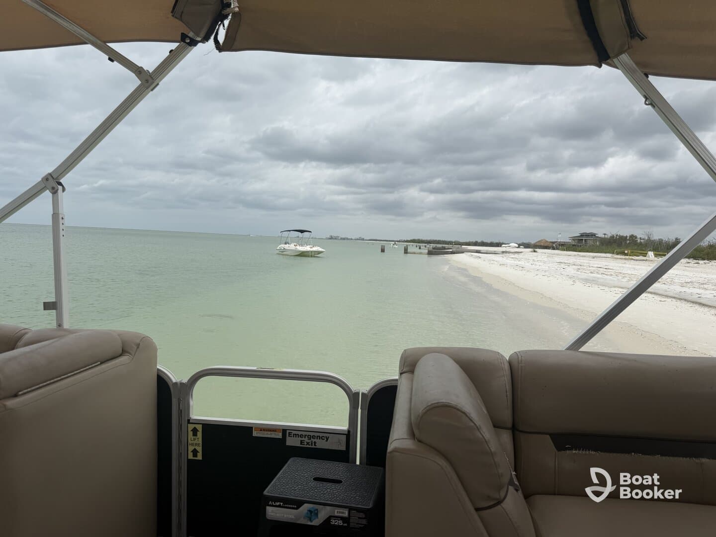 A cozy view from the interior of a pontoon boat, showcasing comfortable seating and a serene backdrop of calm waters and a sandy shore.