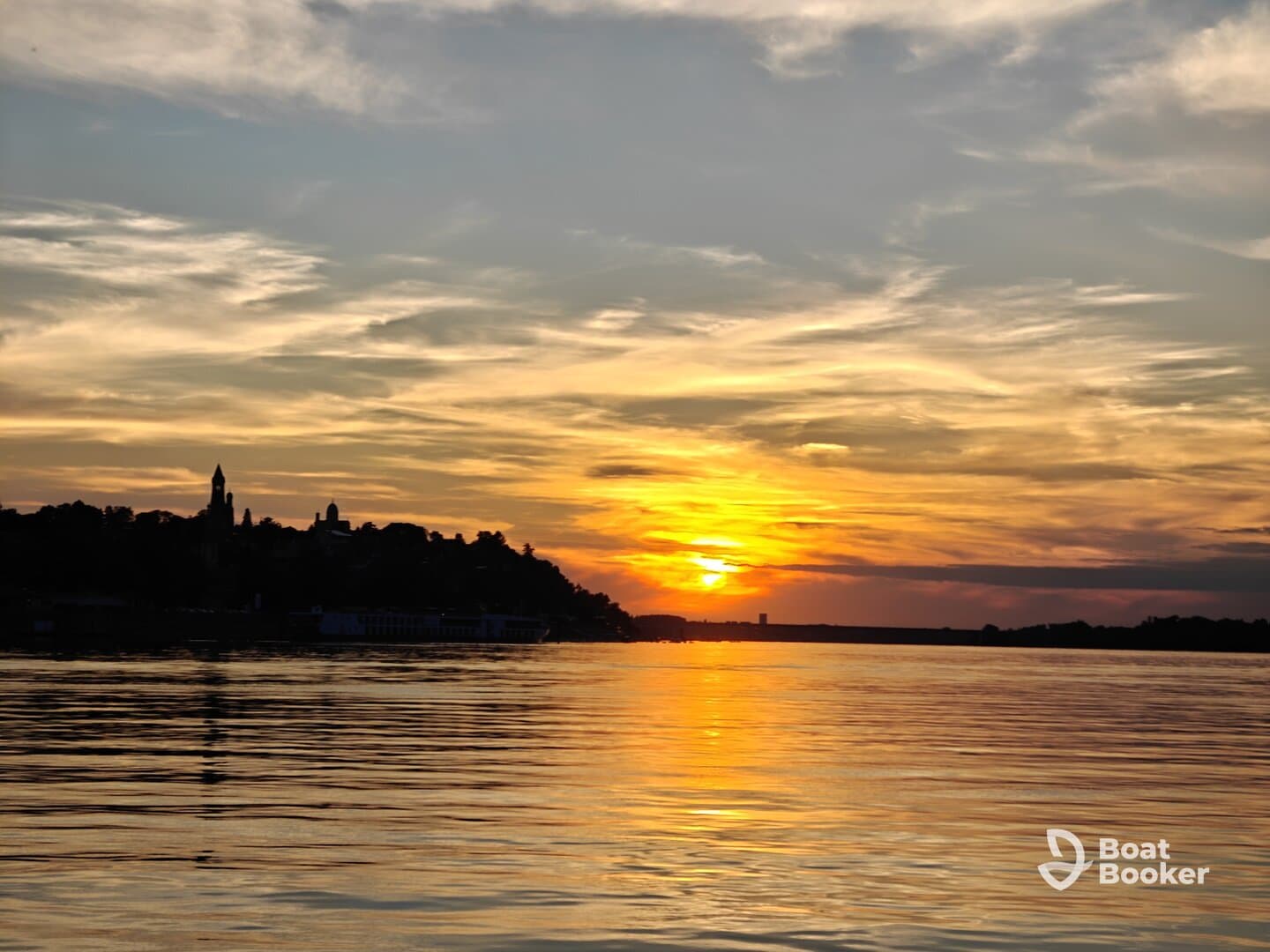 A stunning sunset casts vibrant colors over the water, creating a picturesque view of the coastline — perfect for romantic evenings or scenic boat trips.