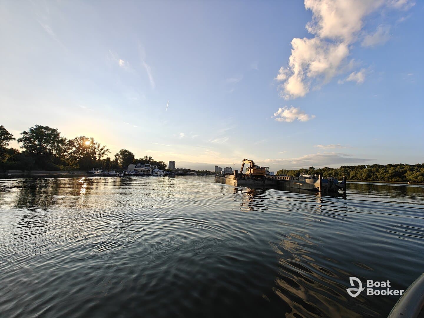 A serene sunset view over calm waters, showcasing the reflection of trees and buildings along the shoreline — perfect for capturing the beauty of nature.