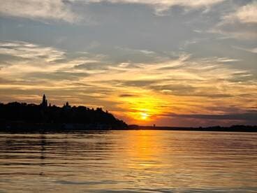 A stunning sunset casts vibrant colors over the water, creating a picturesque view of the coastline — perfect for romantic evenings or scenic boat trips.