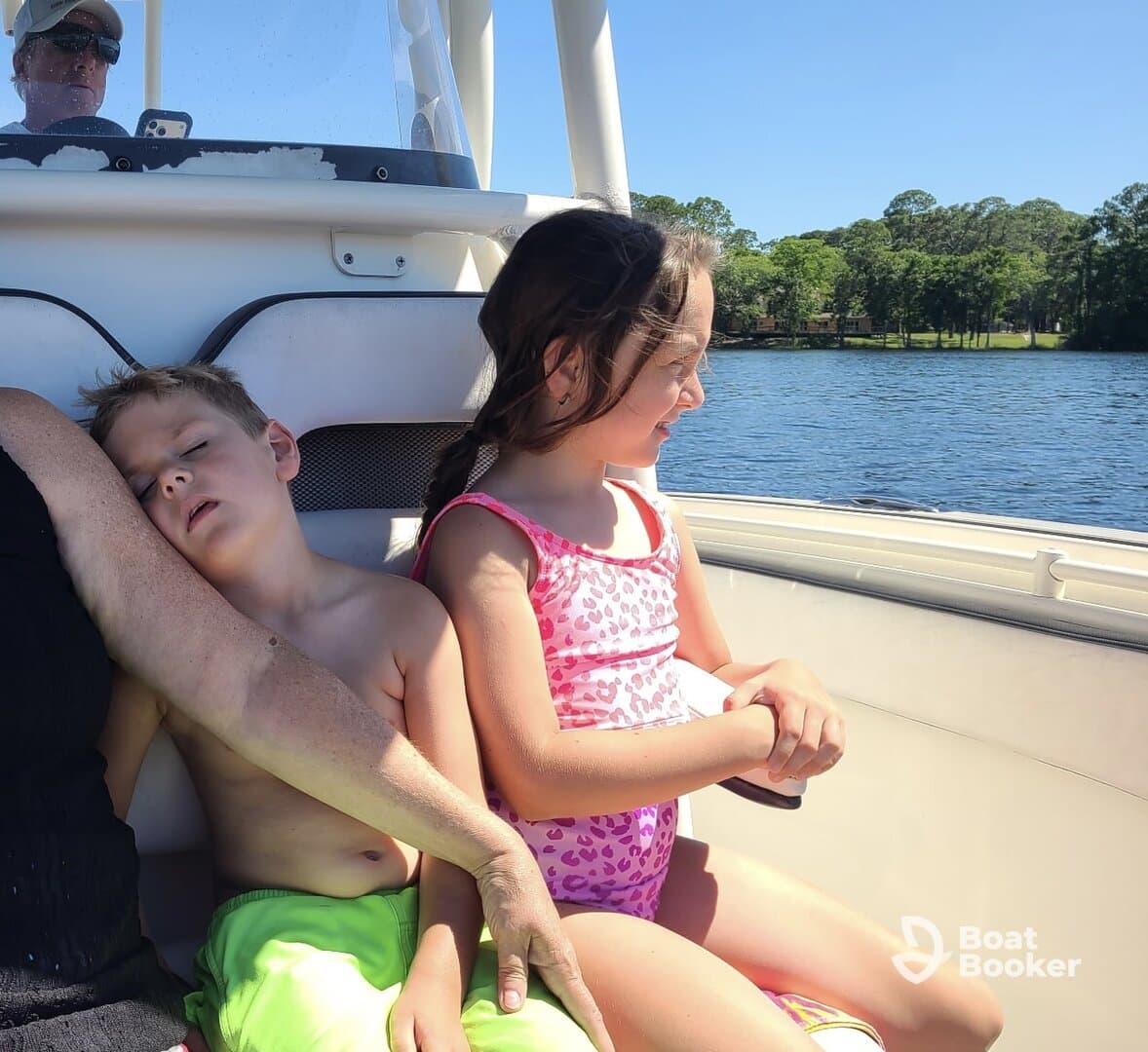 Two children enjoy a sunny day on a boat, with one resting while the other gazes at the water — a perfect family outing on the water.