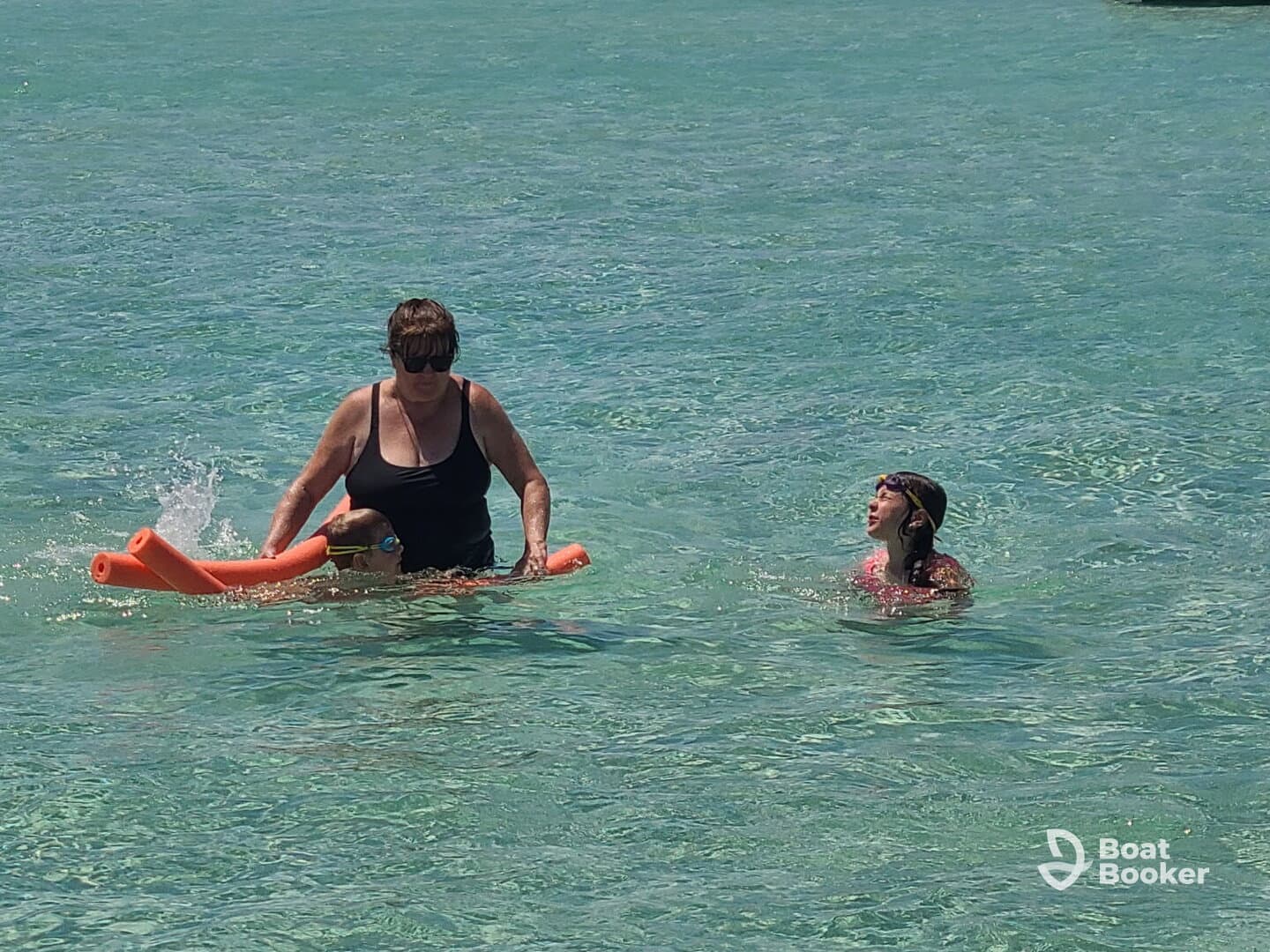 A family enjoys a fun day in the water, with one adult assisting a child on a float while another child swims nearby — perfect for memorable summer adventures.